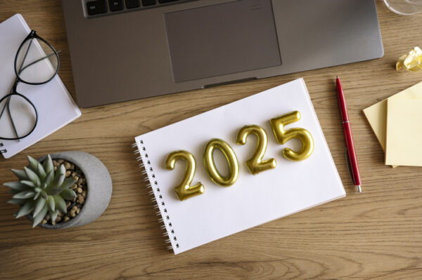 2025 with gold balloon numbers on a white notebook, desk with laptop and accessories.