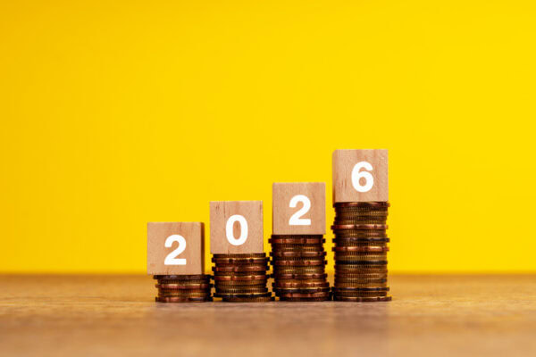 Stacks of coins with wooden blocks displaying "2026" against a yellow background.